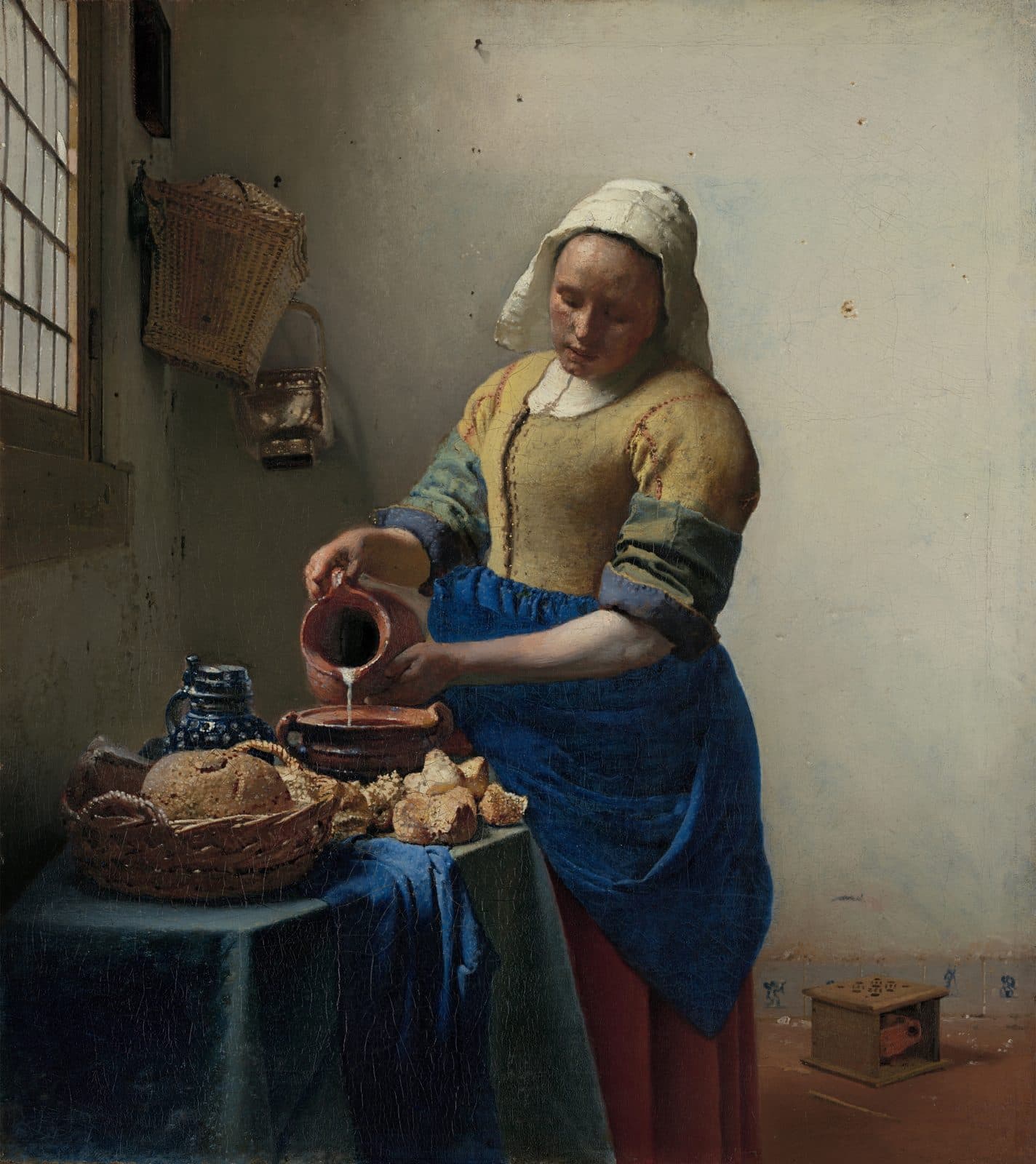 Detail of The Milkmaid: A kitchen maid in a yellow bodice pours milk from a jug into a bowl by a window, bread on the table before her