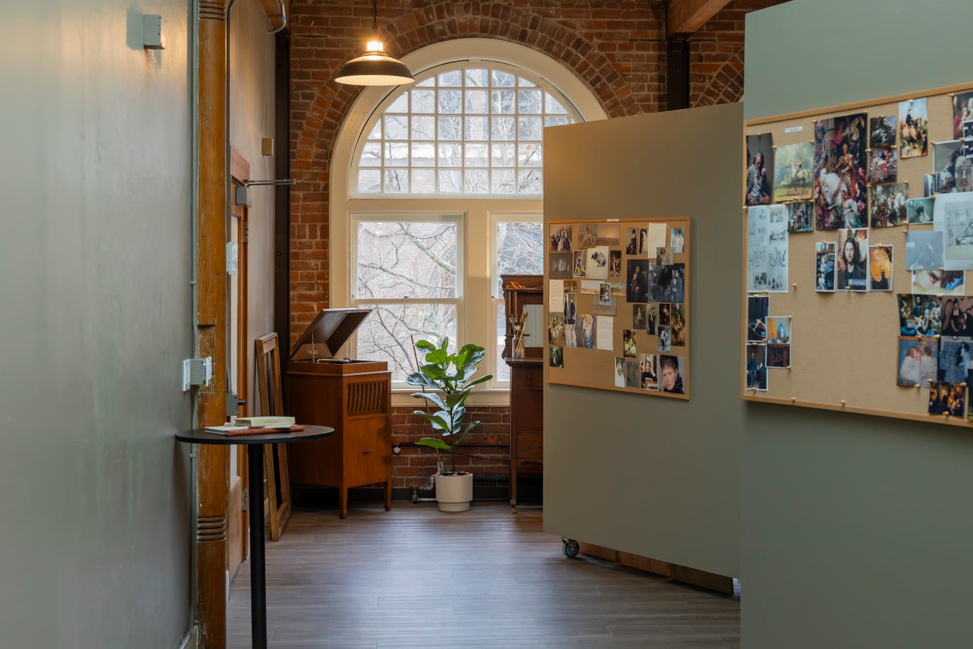A tall arched north-light window inside a third-floor Occidental studio, with brick walls and a photo collage board.