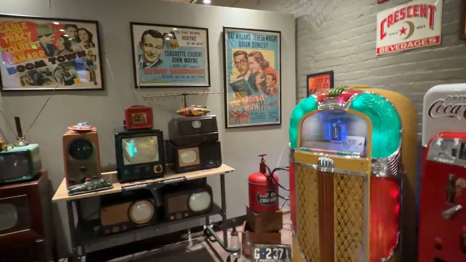 Small 1940s and 1950s television sets on a table under framed movie posters