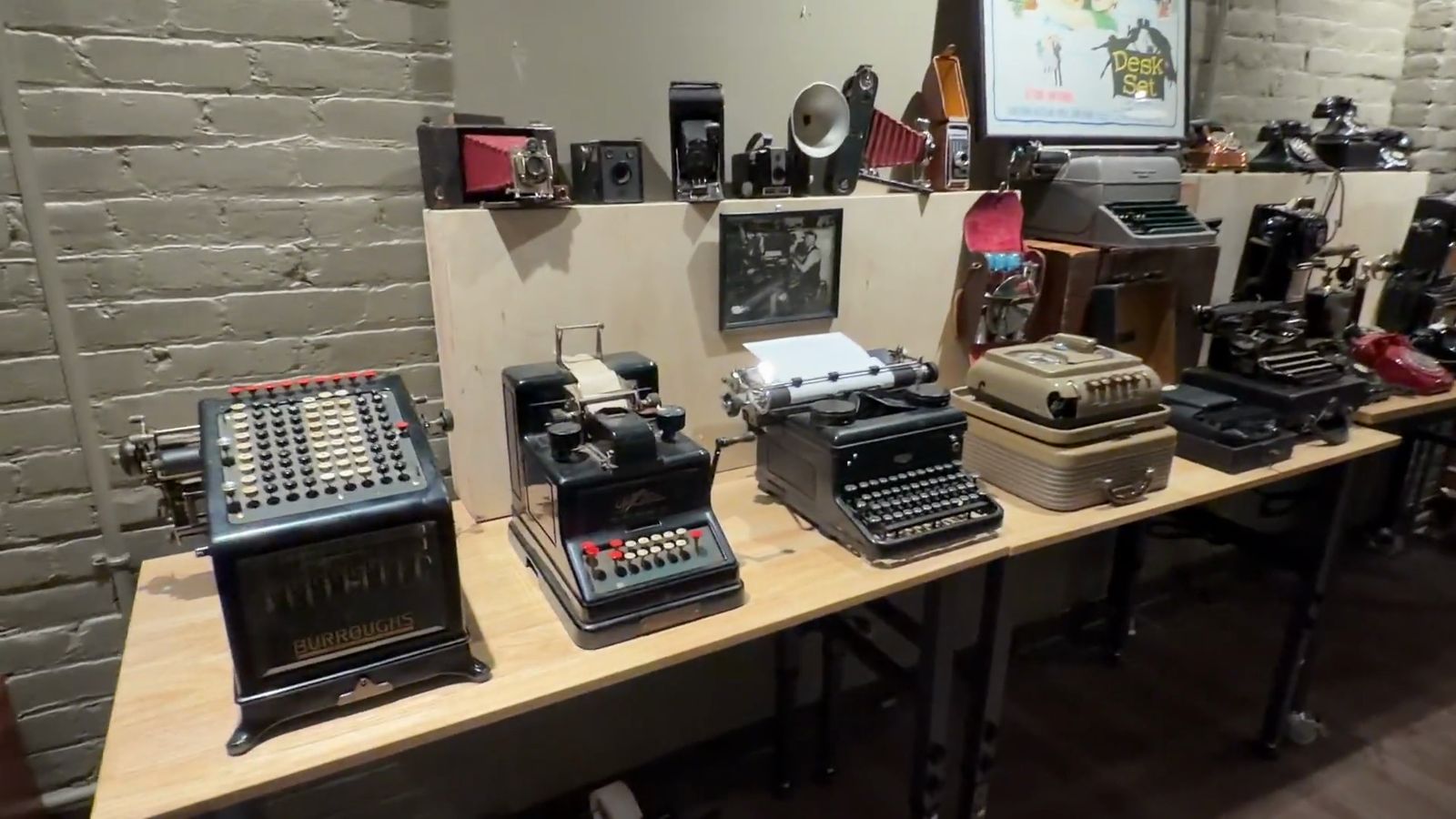 A long table of old typewriters and adding machines in the gallery